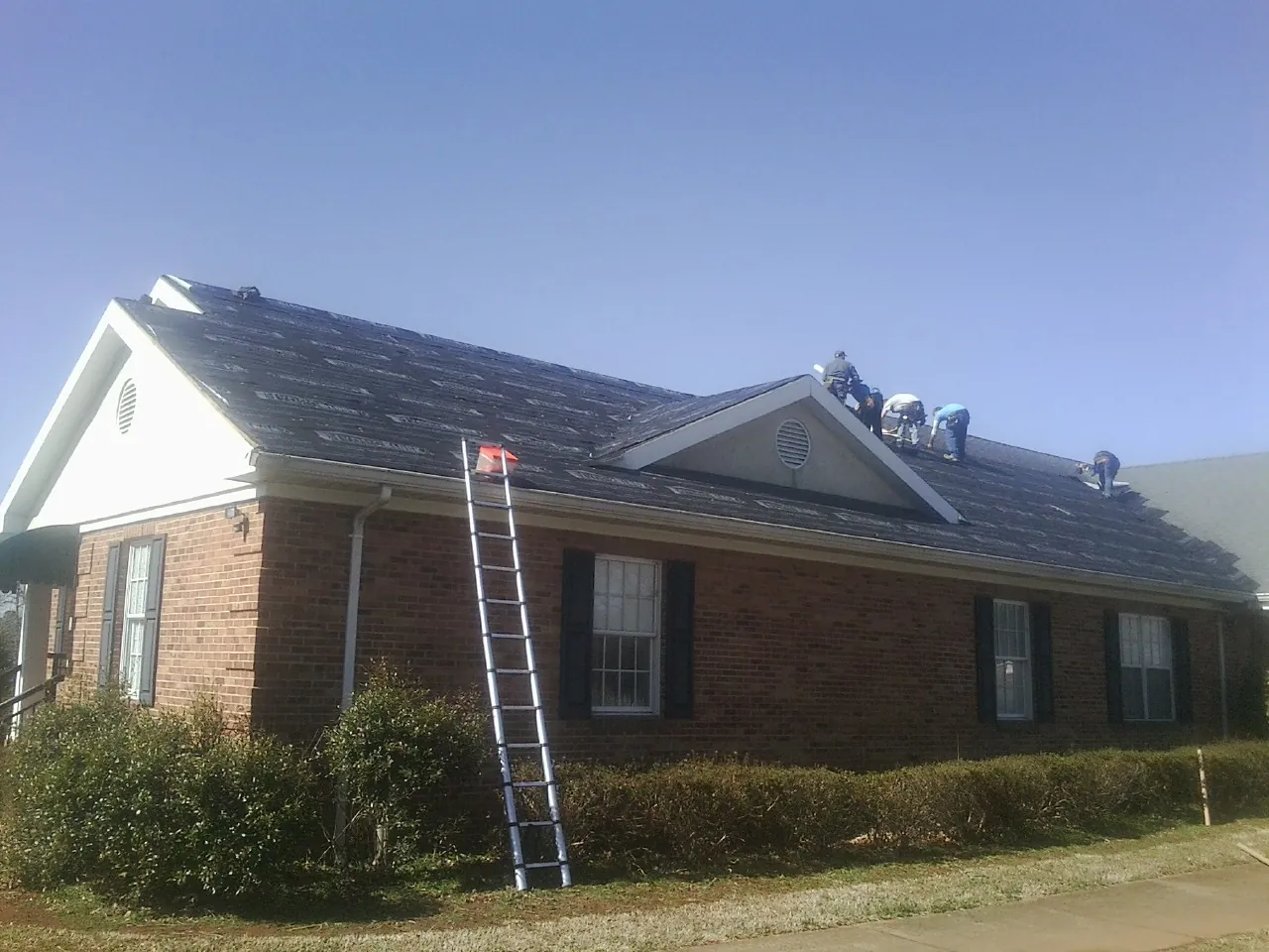 Crew tearing shingles off a brick ranch roof with a ladder set — Emergency Roof Repair work by our crew in Bluffton
